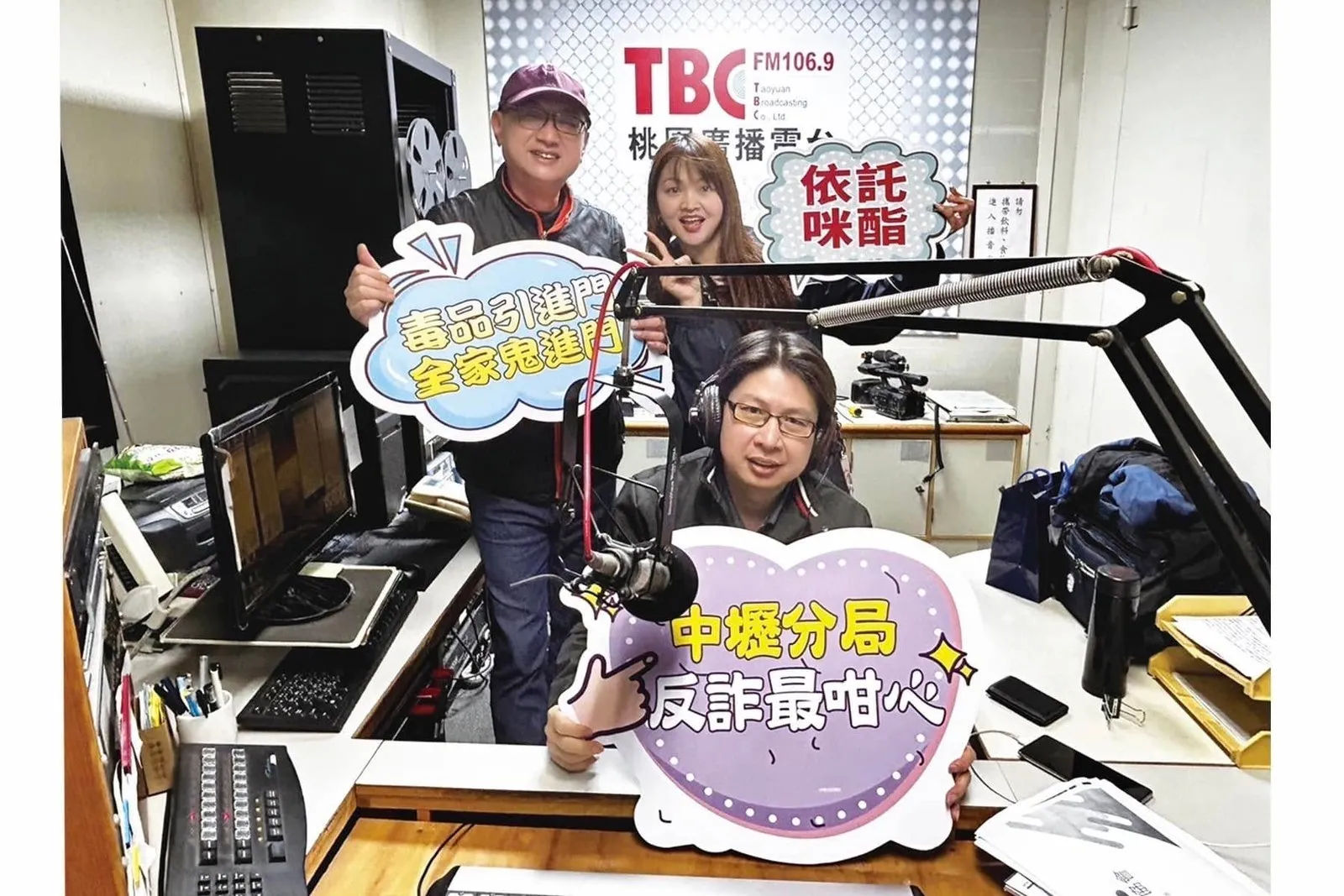 三人在錄音室的混音台前,手持反詐與反毒宣導看板