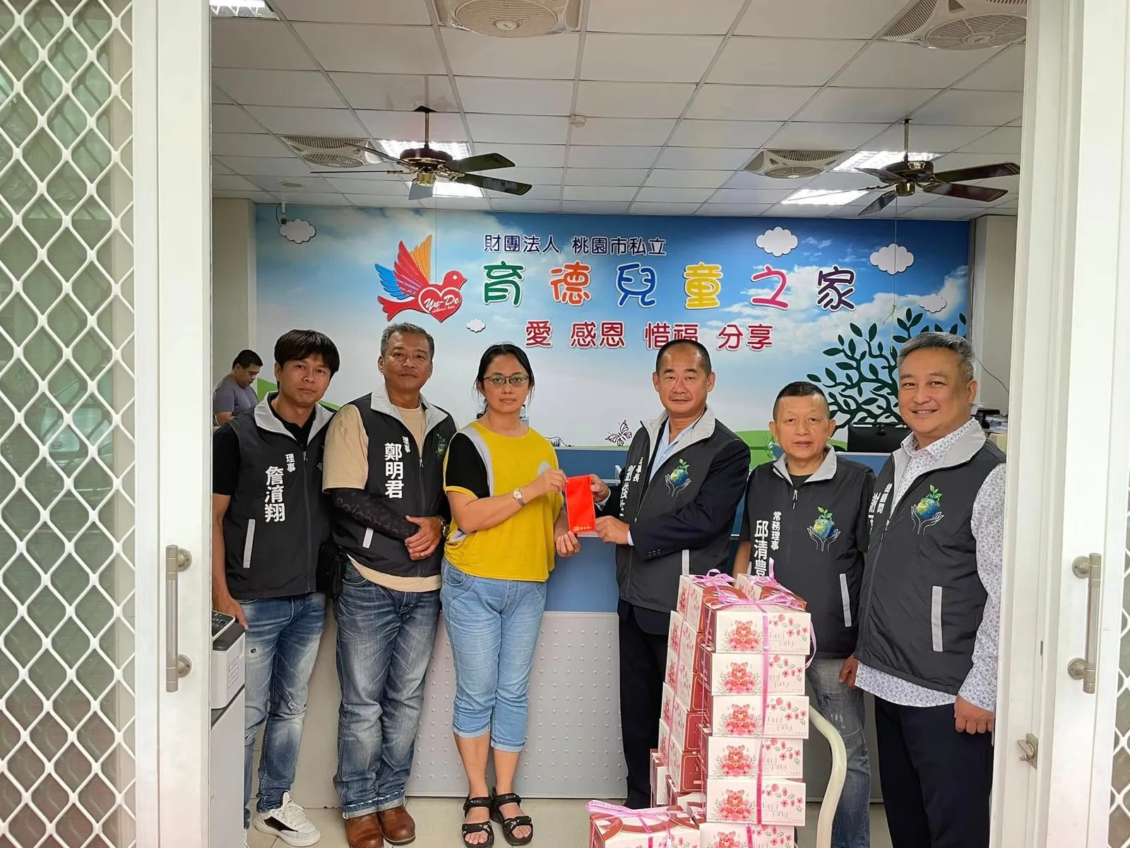 協會幹部與院方人員手捧麵包餐盒,在「育德兒童之家」彩繪牆前合影