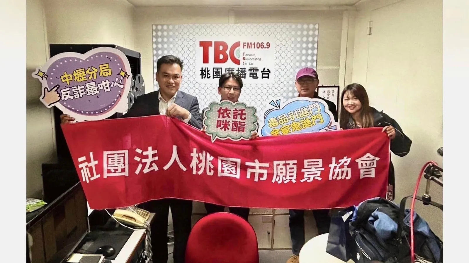 四人在桃園廣播電台錄音室拉開協會布條，手持反詐與反毒宣導看板合影