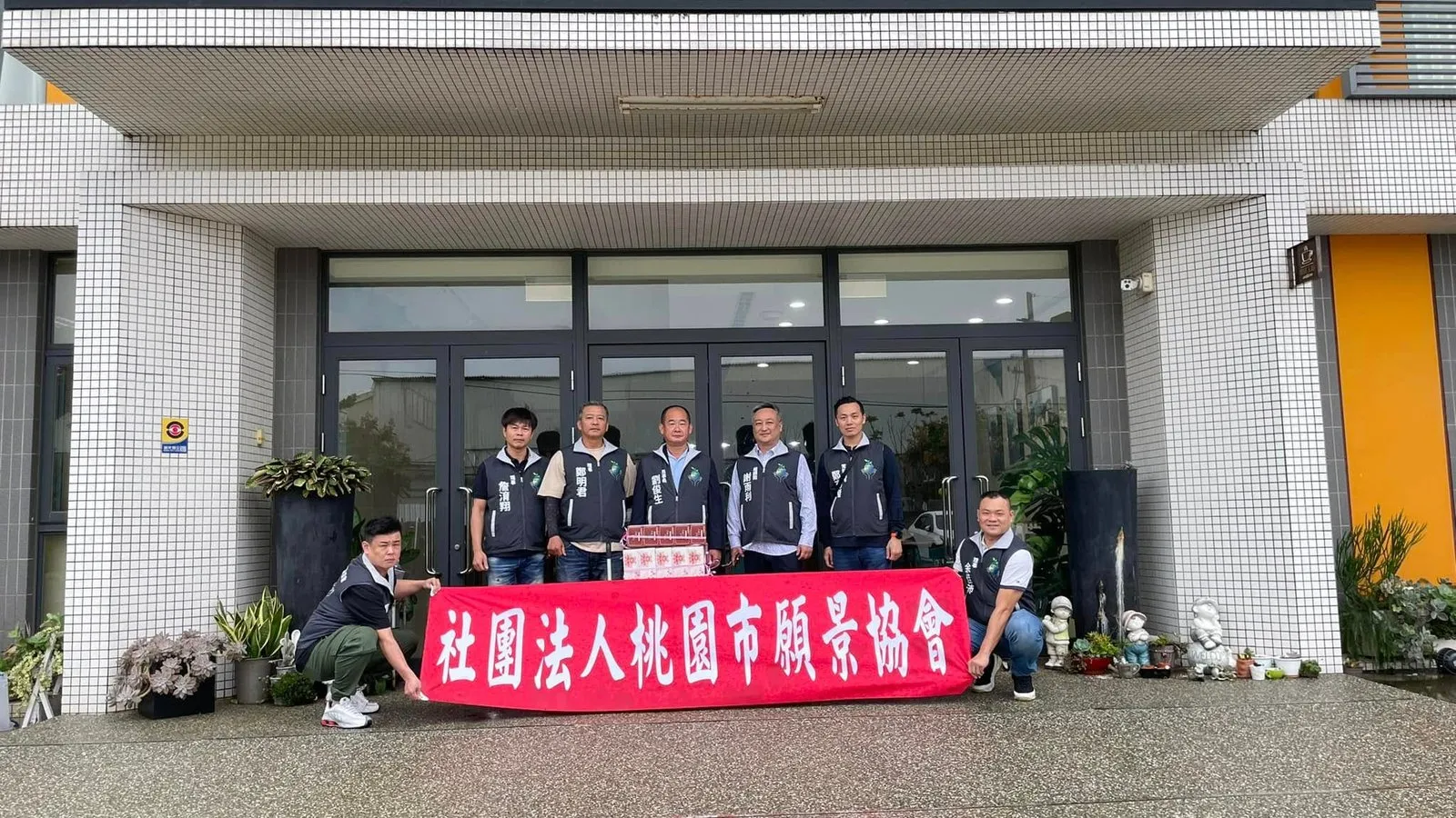 協會幹部在藍迪兒童之家門前拉開「社團法人桃園市願景協會」紅色布條合影
