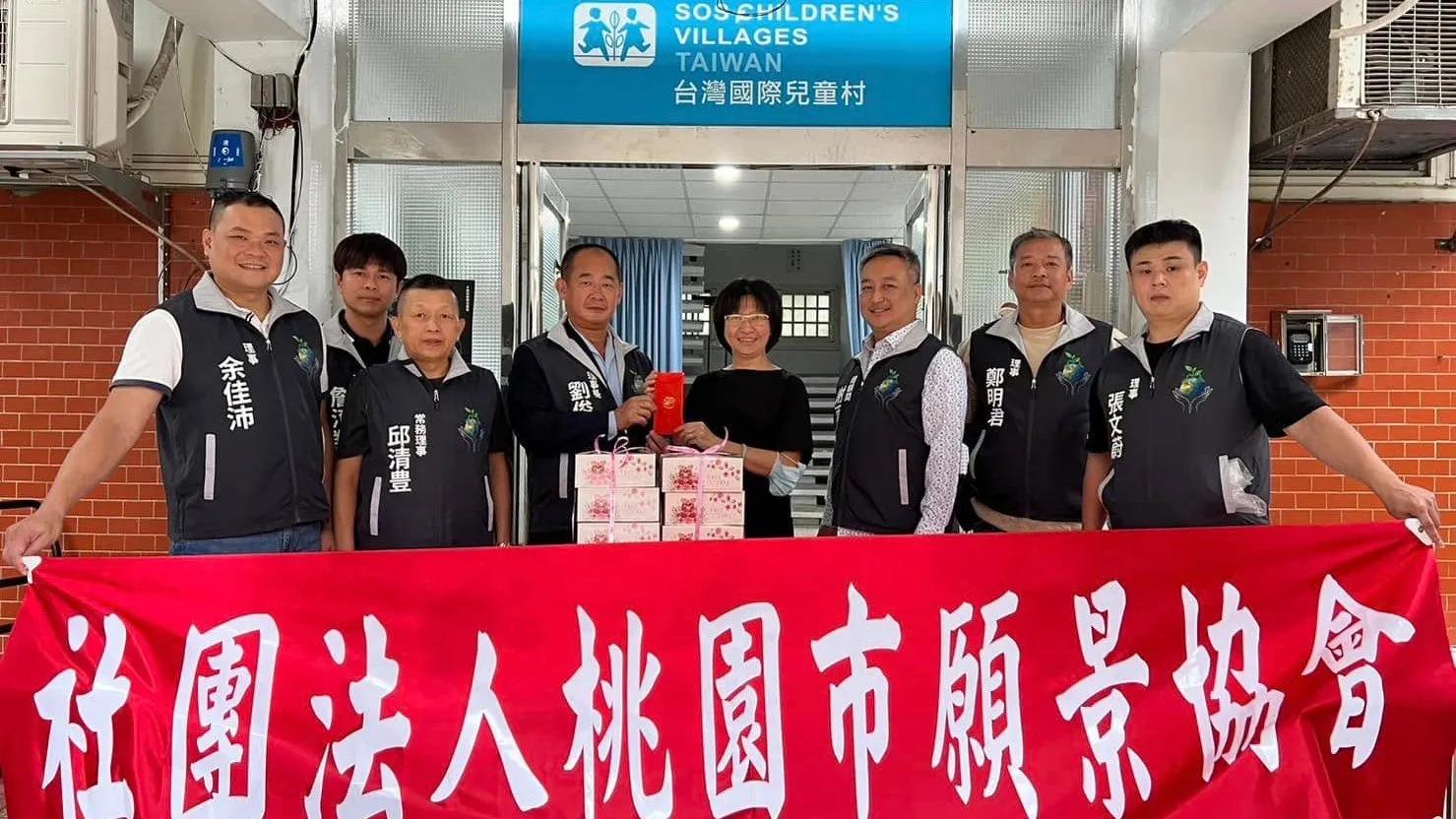 協會幹部在台灣國際兒童村門口拉開紅色布條，與院方代表合影，門楣上有兒童村的標誌