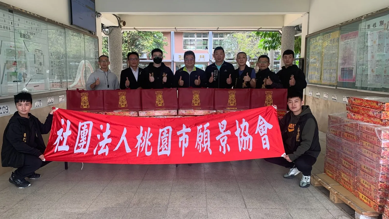 協會成員在建國國中走廊拉開紅色布條合影，身後是堆放整齊的捐贈物資